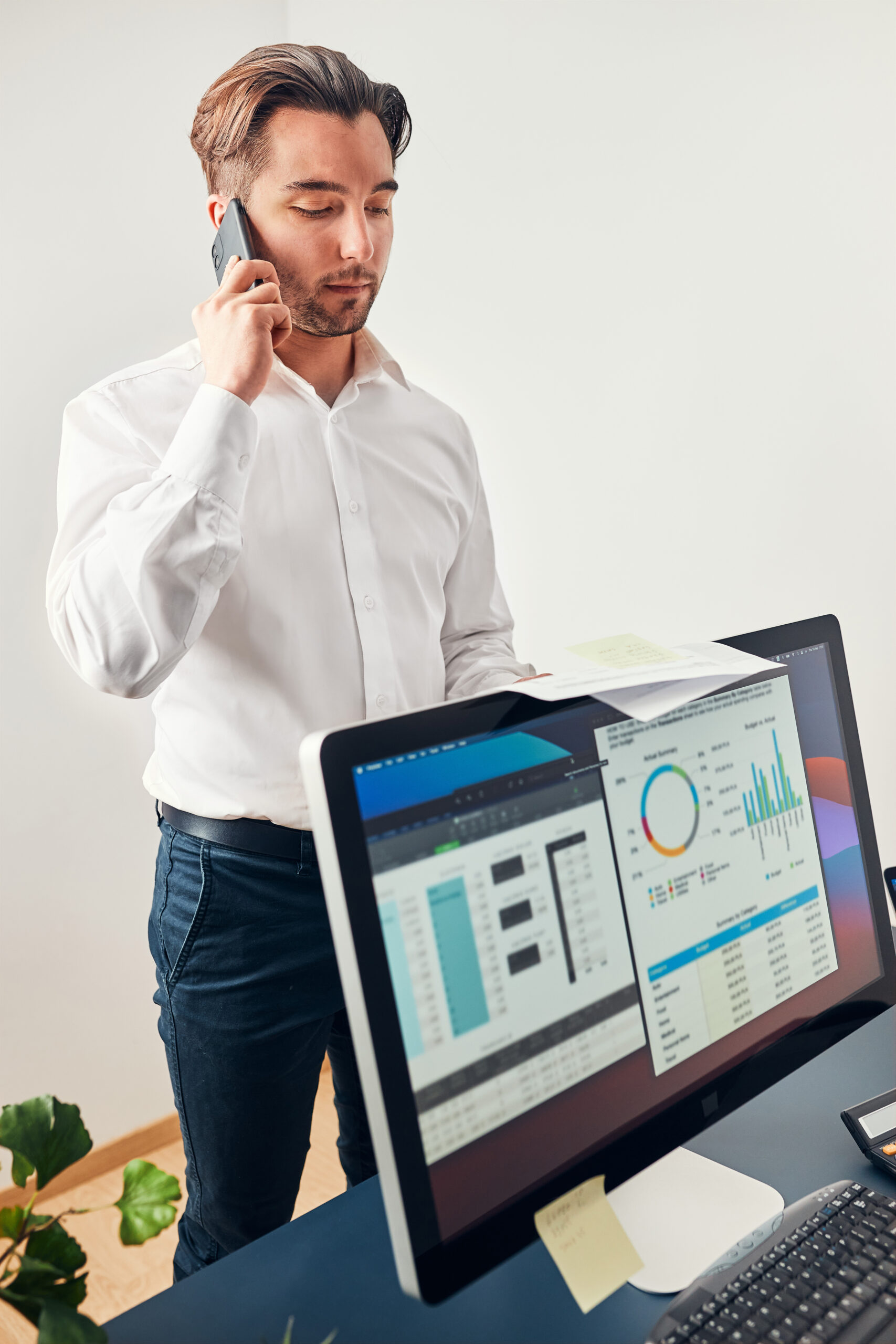 Man entrepreneur having business  conversation on mobile phone. Businessman holding documents and smartphone working with data on charts and graphs in office. Man standing at desk